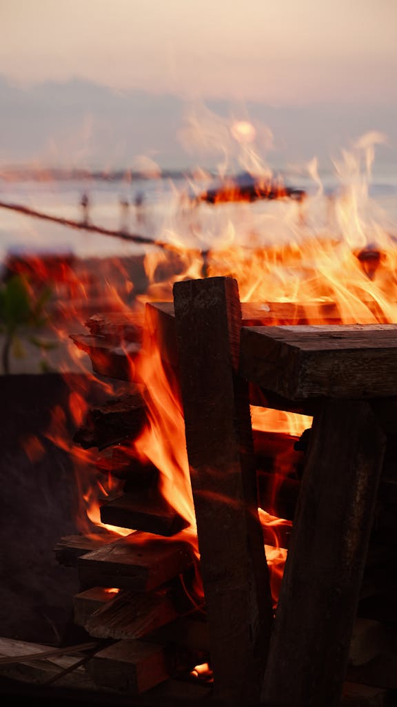 Warm bonfire on a beach creating a vibrant glow at sunset.